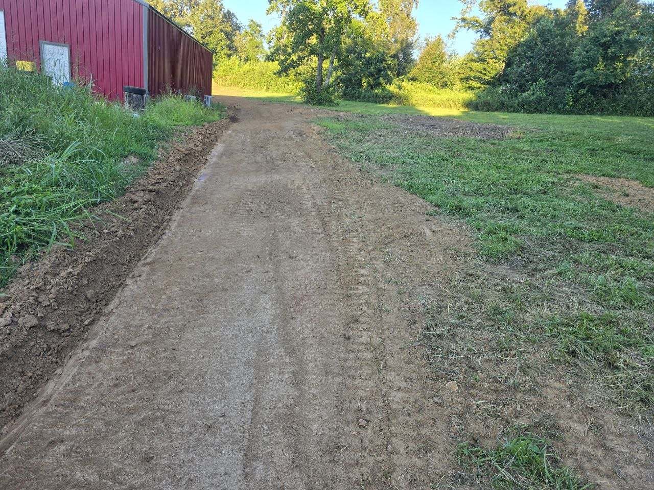 Graded drainage ditch and lane beside a red metal shop building