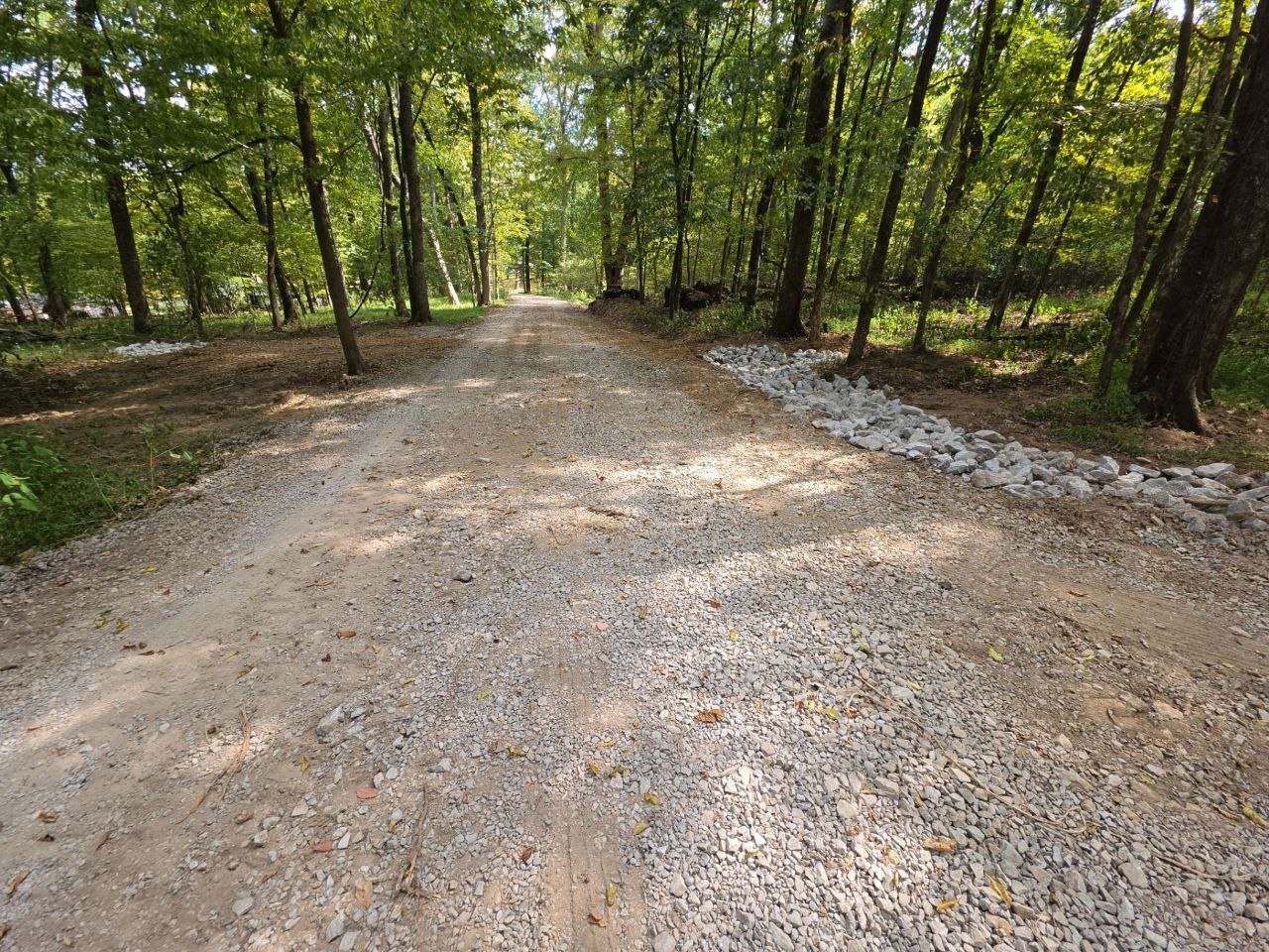 Finished gravel driveway with a stone-lined drainage edge through the woods, Pulaski TN